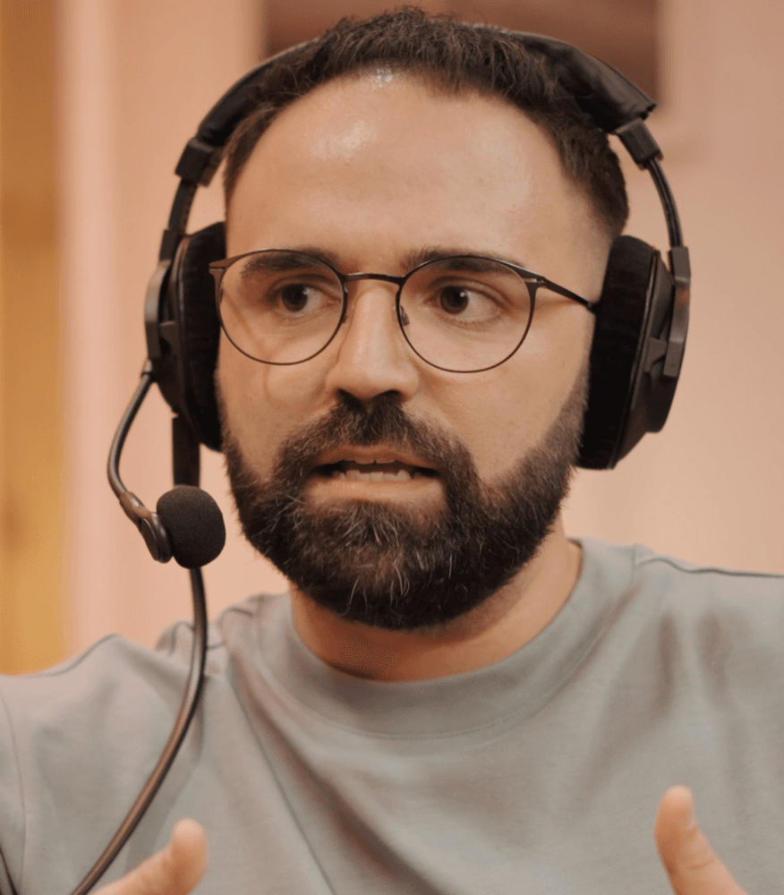 Podcast-Foto: Mann mit Brille und Headset-Mikrofon spricht und gestikuliert