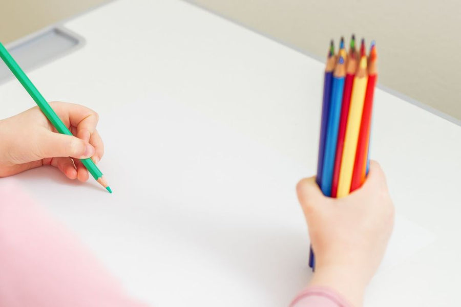 Foto: Kinderhand malt mit einem grünen Buntstift, die andere Hand hält bunte Stifte