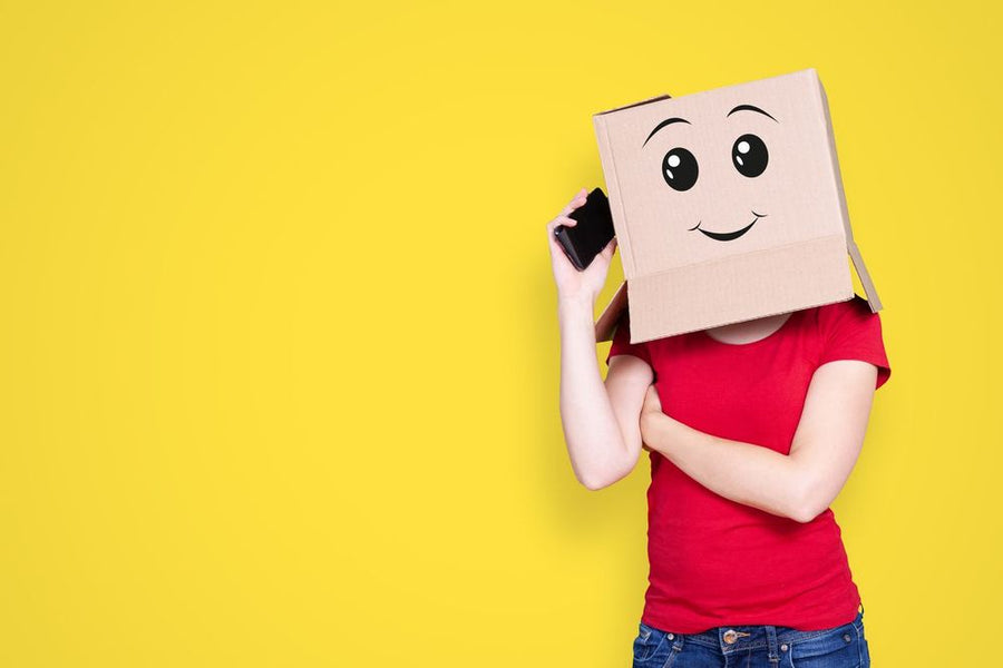 Foto: Person mit einem Karton mit aufgemaltem Smiley über dem Kopf hält ein Smartphone ans Ohr