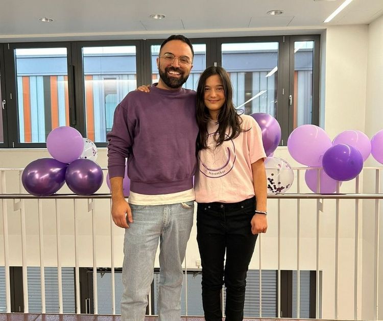 Foto: Ein Mann und ein Mädchen stehen lächelnd nebeneinander, im Hintergrund lila und weiße Luftballons
