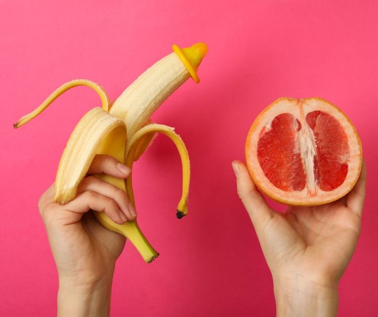Foto: Zwei Hände halten eine geschälte Banane und eine halbierte Grapefruit vor pinkem Hintergrund