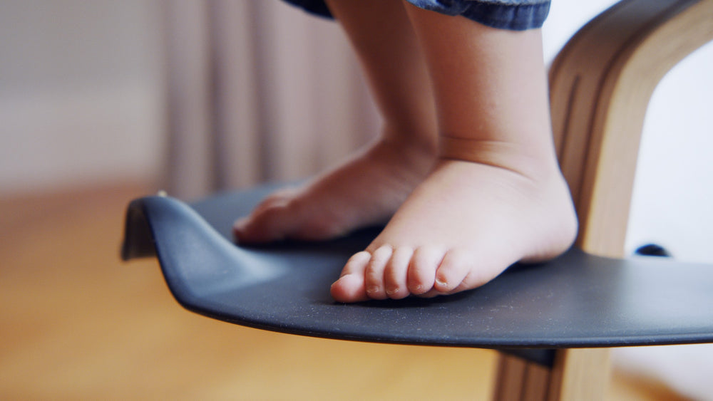 Nackte Kinderfüße auf der Fußstütze eines Hochstuhls