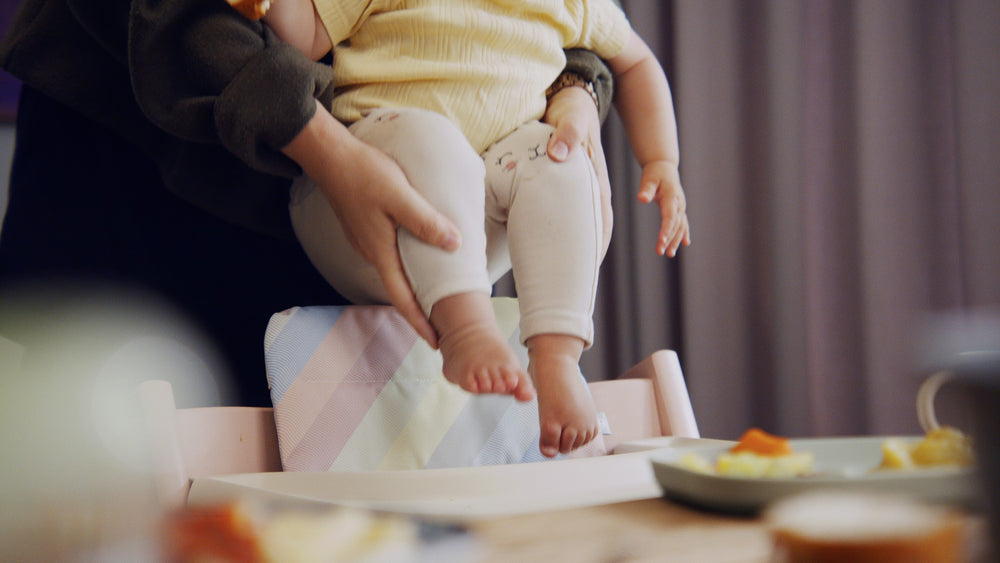Baby sitzt auf dem Schoß am Esstisch, die Füße baumeln