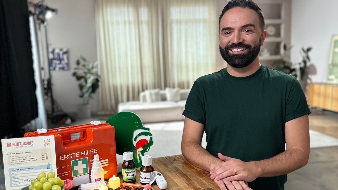 Kinderarzt Dr. Vitor Gatinho am Tisch mit Erste-Hilfe-Koffer und Notfallkarte