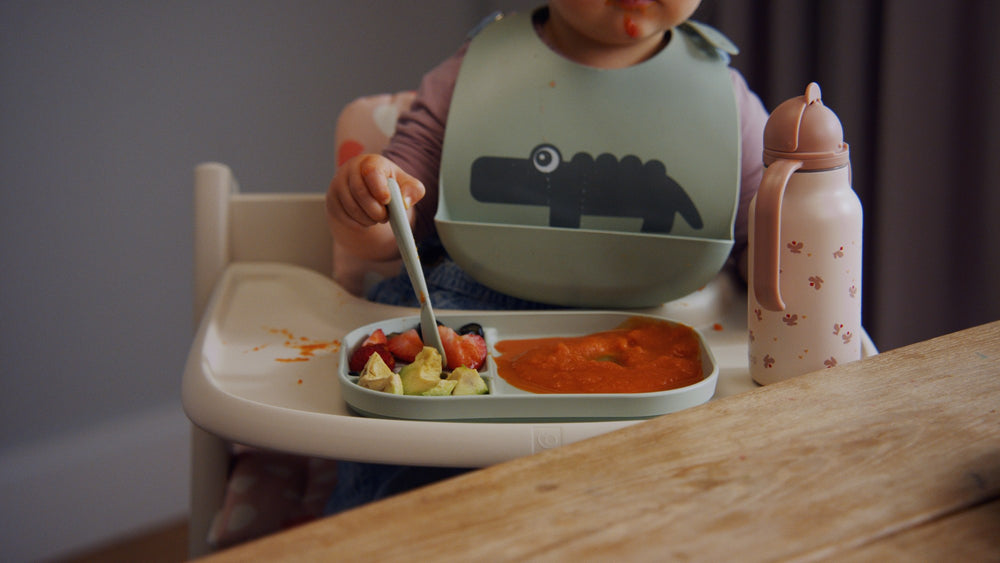 Kleinkind mit Lätzchen isst am Tisch im Stokke Hochstuhl mit Tablett