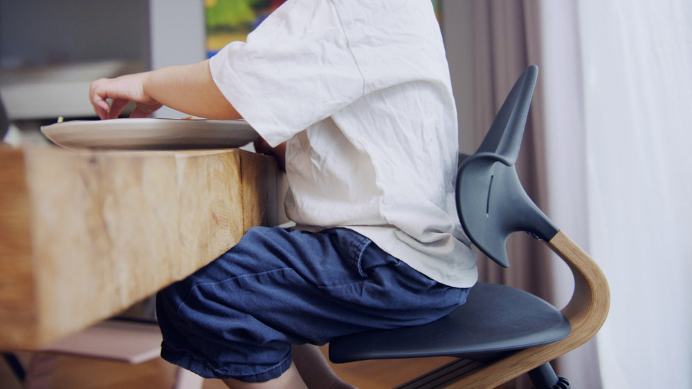 Kind sitzt am Tisch auf dem Stokke Nomi Stuhl, Seitenansicht